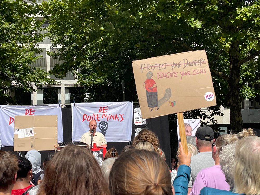 wim vader van sanne op foto rechts staat op het podium tijdens demonstratie te vertellen over de moord op zijn dochter protestbord met protect your daughters doorgestreept educate your sons!