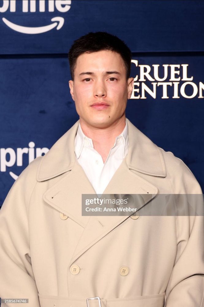 derek luh at the cruel intentions premiere. wearing a long sandy beige overcoat over a white shirt, unbuttoned at the top.