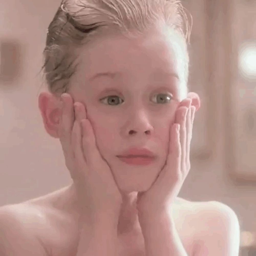 a young boy is making a surprised face with his hands on his face in a bathroom .