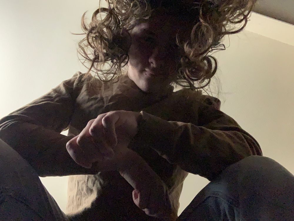 Sam towers over the viewer, her hair cascading over her face as she gives them a smirk cast in shadow. She's squatting, her legs on both sides of the viewer.