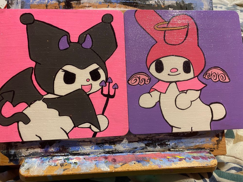 Two wooden panels painted. The one on the left is of the Sanrio character Kuromi with devil horns, a tail and a pitchfork on a bright pink background. The one on the right is of the Sanrio character My Melody with a golden halo and pink wings on a light purple background. They are meant to be hung together. 