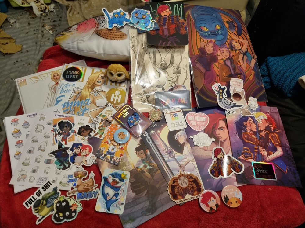 Picture of our combined haul, showing even more stickers, some extra prints, two comics, a little barn owlet figure and a rainbow trout plushie which has been named Harry by my partner