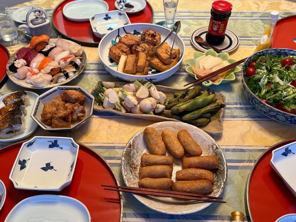 a table served with salad, grilled vegetables, fried chicken, and three kinds of sushi 