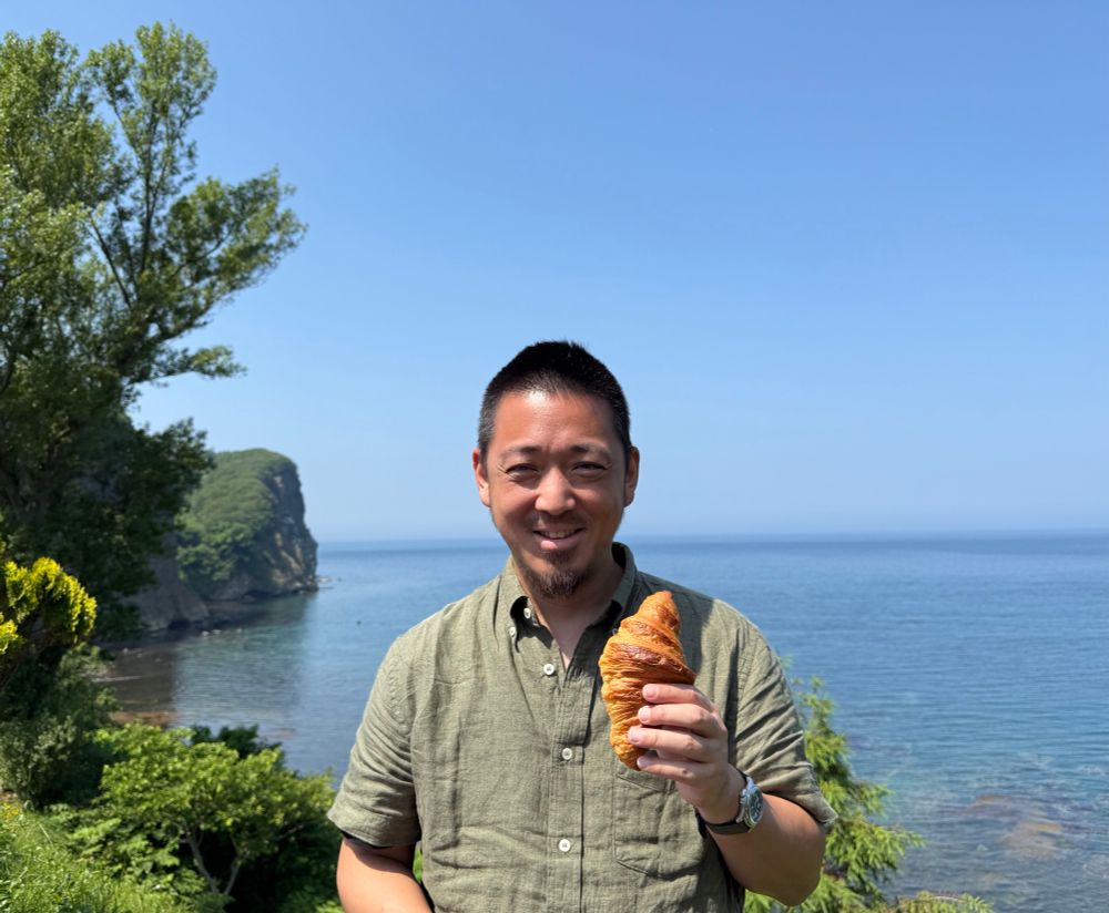 a bozo posing with a croissant with the ocean in the background