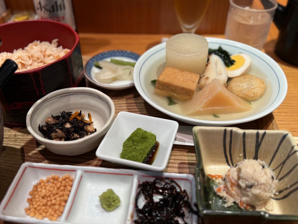 a bowl of oden (vegetable and fish cake stew) served with small plates of sides and rice