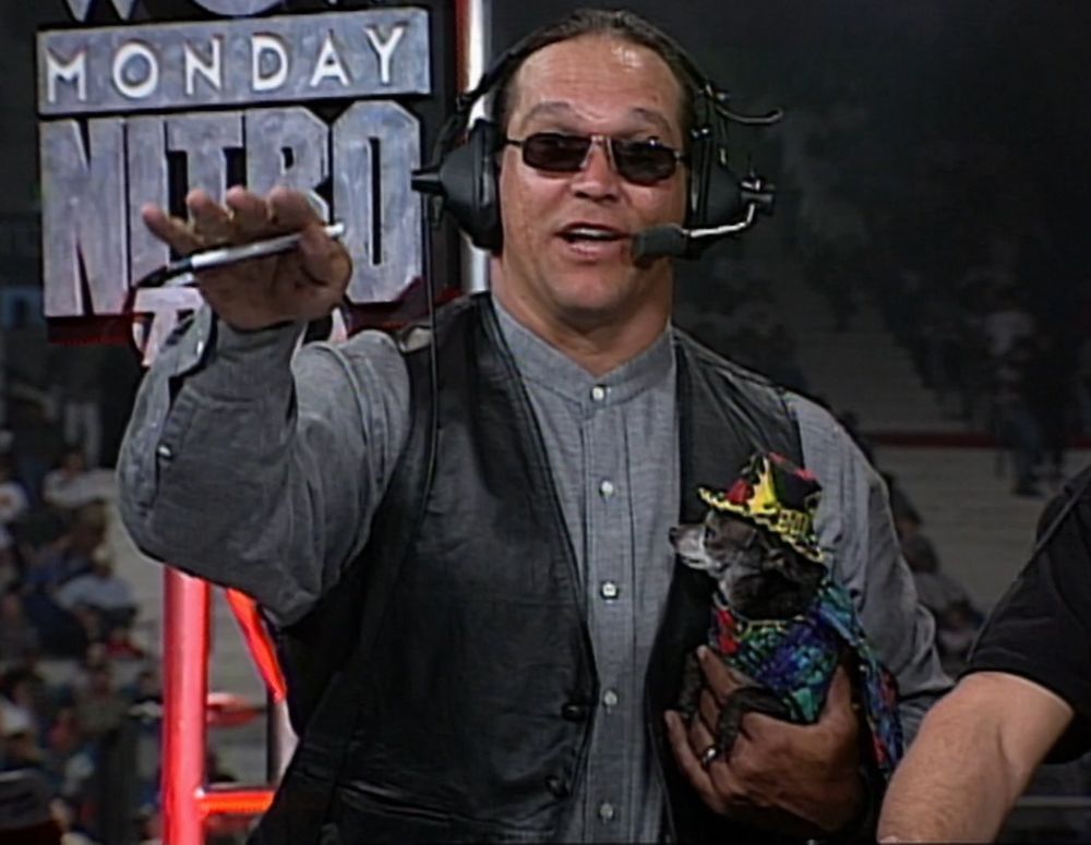 a close-up of mongo holding pepe, who has a very colorful patterned coat on and a colorful hat on, both are reminiscent of "macho man" randy savage's gear style and the hat has a batman logo and says BATMAN on the back