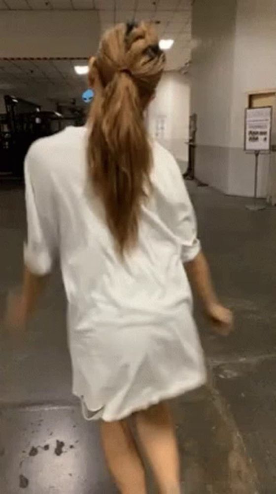 a woman in a white shirt is walking down a hallway