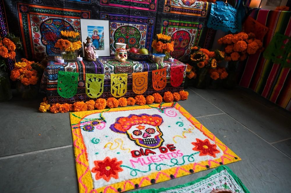 Offrenda with sand art that spells out Dia De Muertos and a sugar skull