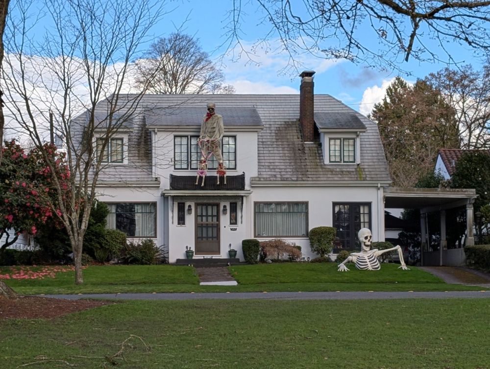 A house with a skeleton hanging above the front door, and a decoration on the front lawn that looking like a giant skeleton coming out of the ground.