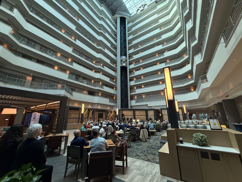 a jazz band plays to a largely seated at table audience in a tall hotel atrium with many floors