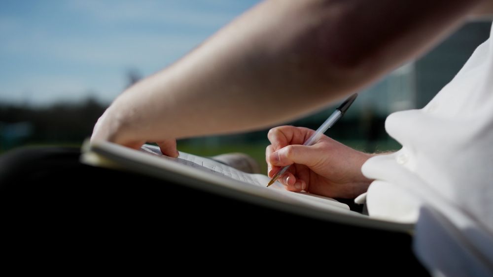 Someone using a pen and notepad to write outside.