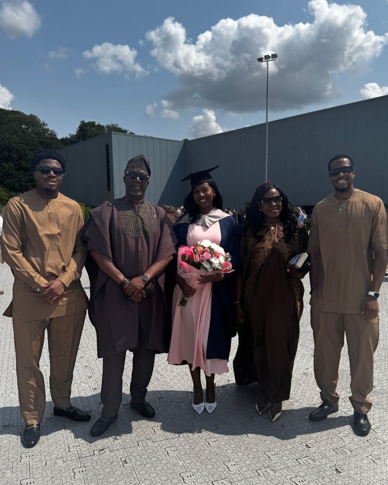 A graduate and their family are standing together and smiling. The graduate is in the middle, with her parents either side, and other members of the family beside them.