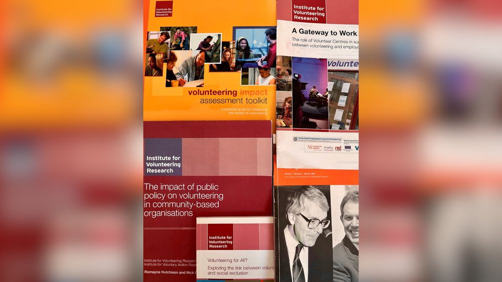 Informative display featuring various posters about volunteering and its impacts, with specific focus from the Institute for Volunteering Research. The background includes a collage of images showing people in different volunteer settings.