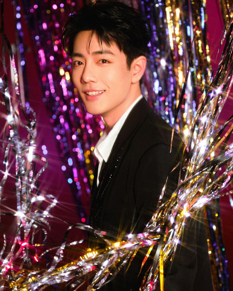 Xiao Zhan in a black suit surrounded by sparkling metallic string