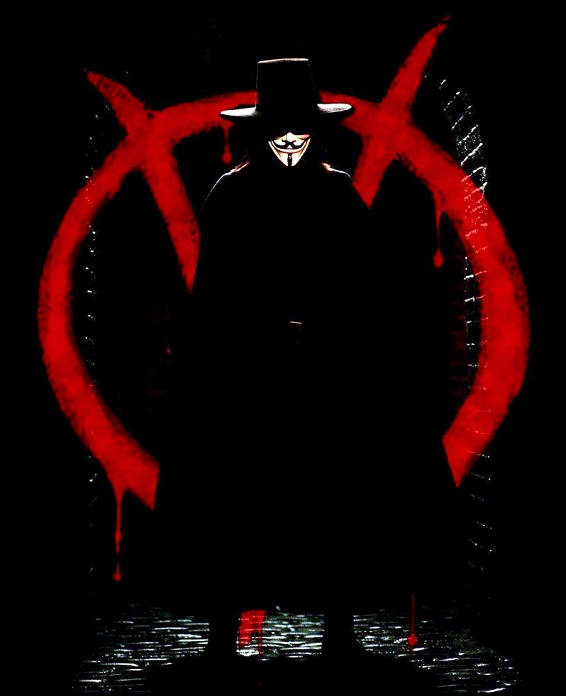 A dark, shadowy figure wearing a Guy Fawkes mask, wide-brimmed hat, and long black cloak stands in front of a large red “V” symbol painted on a wall, with the paint appearing to drip. The scene is dimly lit, creating a dramatic and mysterious atmosphere.