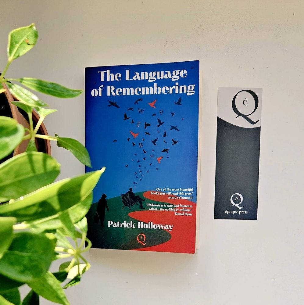 A book flatlay on a white table with green leaves from a plant and a bookmark.
The book is The Language of Remembering by Patrick Holloway 