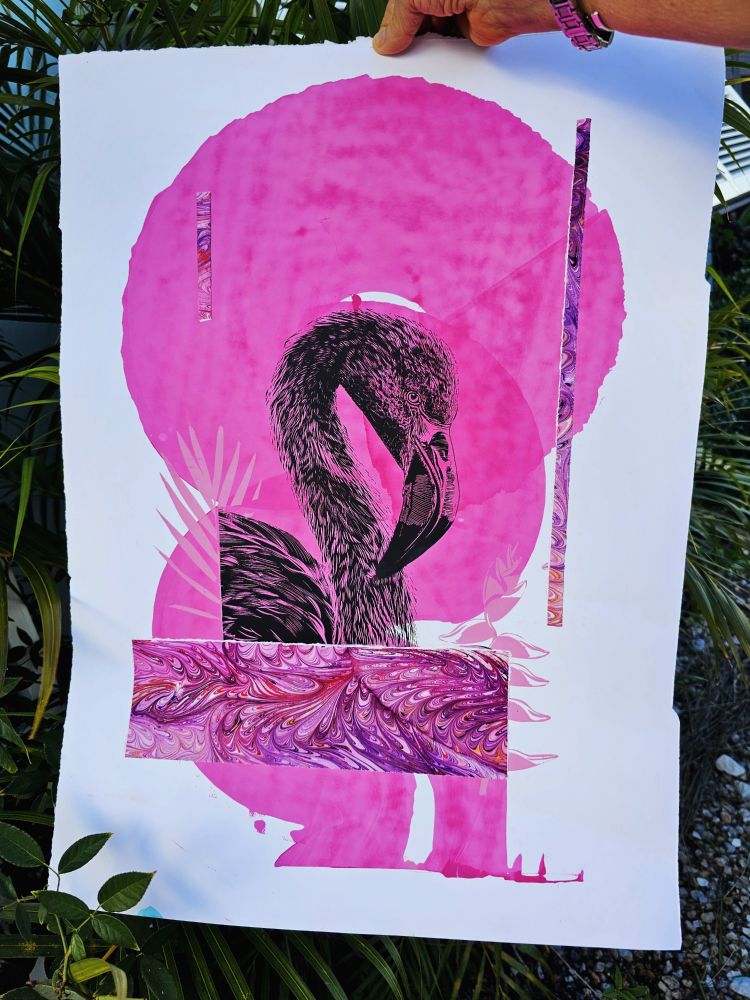 A hand holding a print of a flamingo in black ink. A large swirl of pink ink in round shapes behind it 