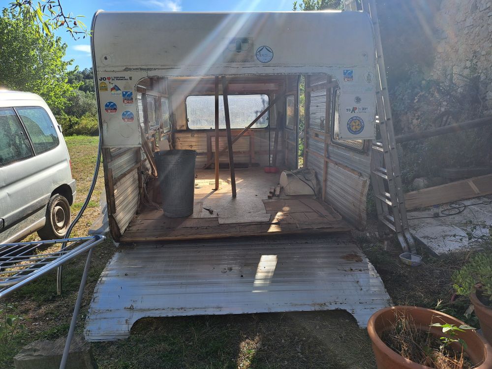 Vista de la caravana por detrás. Se ve una parte de la pared de chapa en el suelo.