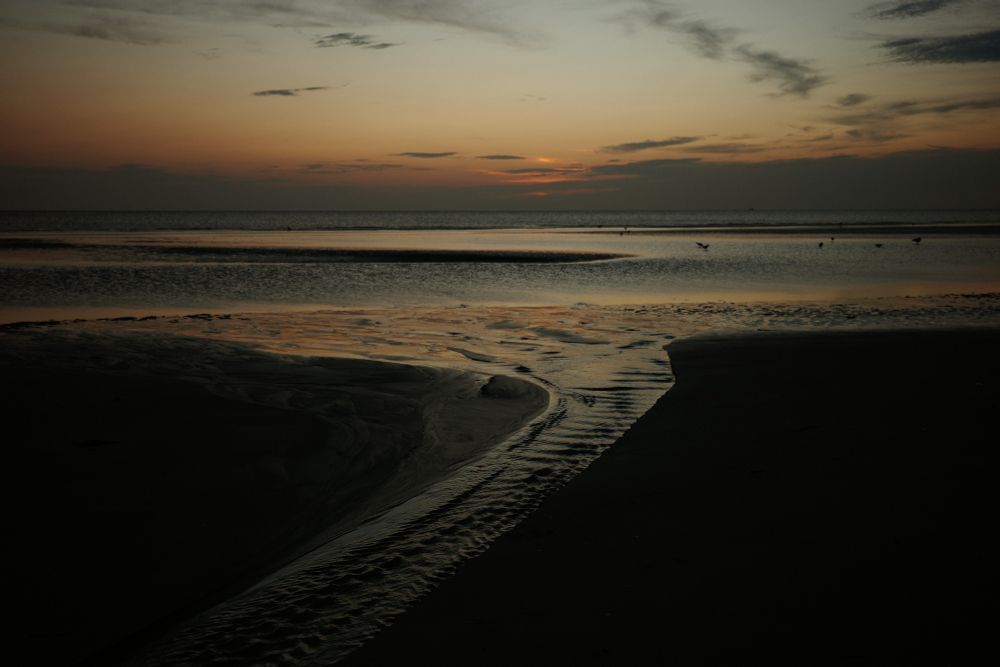Sonnenuntergang am Strand. Im Vordergrund kleine Flüsse.