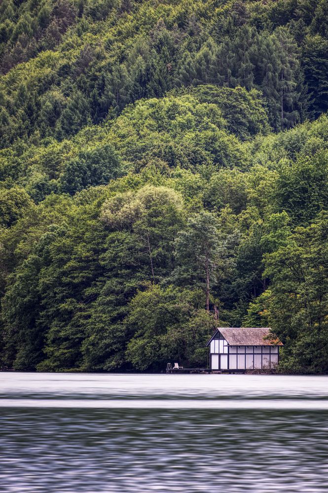Image shows a lone boathouse at a lake with forest all around. 