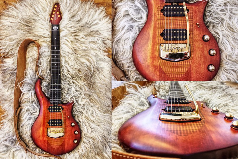 Image shows a 7 string electric Music Man guitar. The guitar is made out of mahogni with gold hardware including tremolo. 