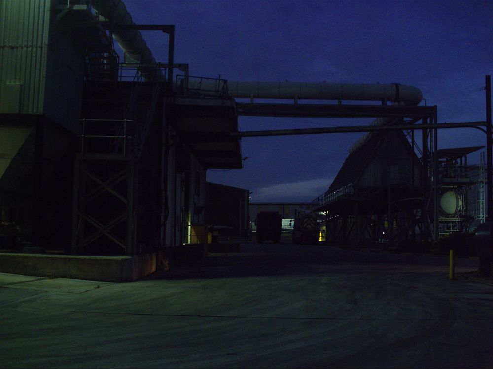 Close up of a dark, dimly lit industrial area. The sky is a dark blue