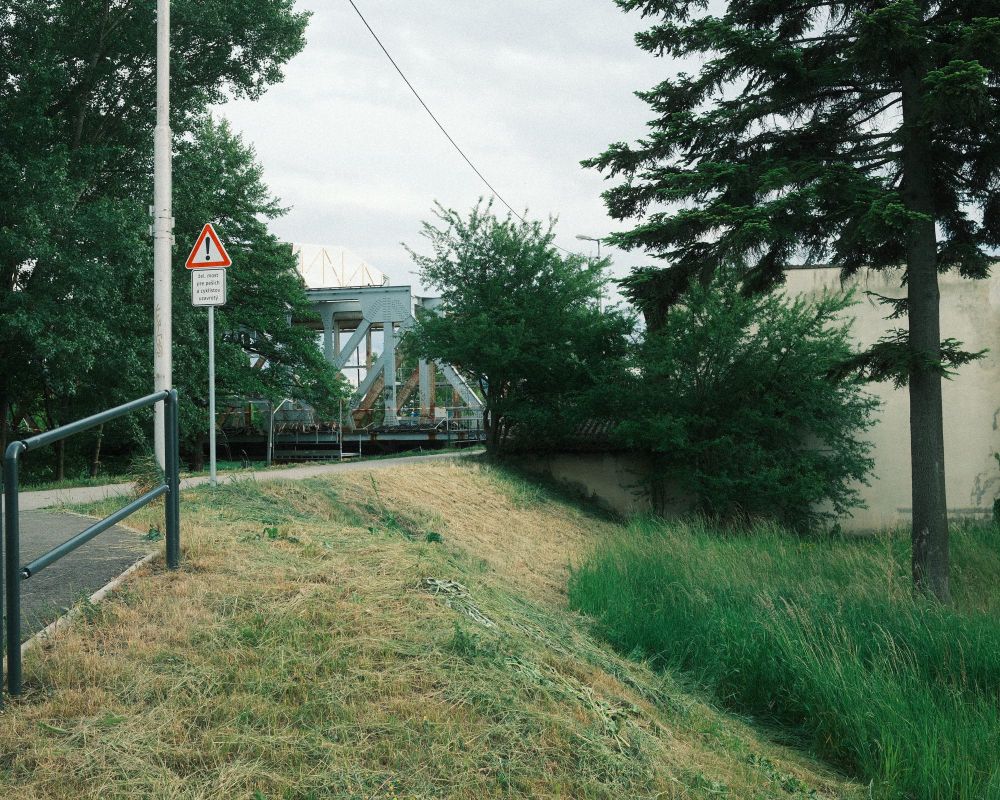 Up on an embankment, some overgrown trees and bushes hide an old iron rail bridge in the distance