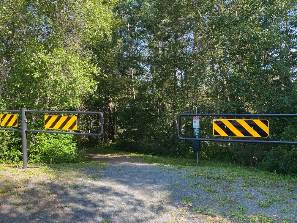 Barriers to stop vehicles entering at the trail head. Signpost and trees. Sunshine through the trees creating "dappled shade".