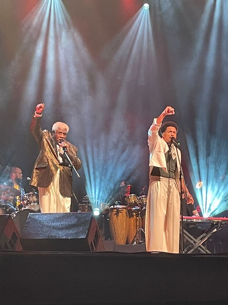Foto do palco com Toni Tornado, a esquerda e seu filho Lincoln com punhos cerrados. 