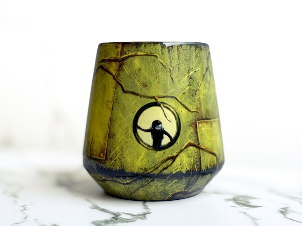 Angled cup featuring weathered spacecraft design and small round window in center showing astronaut looking out at branches wrapping around craft. 