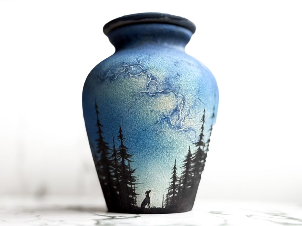 Urn with lid featuring silhouette of a dog looking up toward the Milky Way in the parting of a forest. 