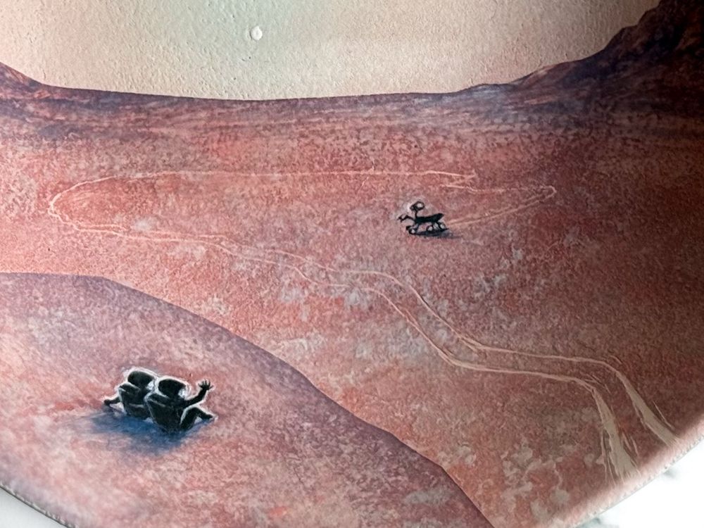 Bowl featuring two astronauts in the foreground sitting on Mars at sunset waving at a rover that travels inside a canyon followed by its own tracks and looks back at them. (Detail of figures)