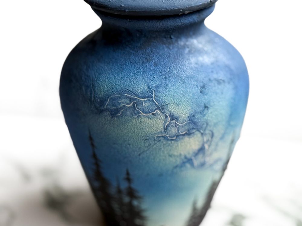 Urn with lid featuring silhouette of a dog looking up toward the Milky Way in the parting of a forest. Detail of Milky Way.