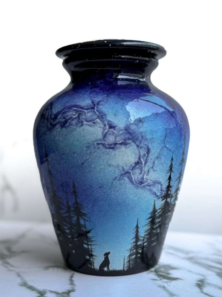 Urn featuring the Milky Way over a silhouette of a dog looking up through the clearing of a forest. 