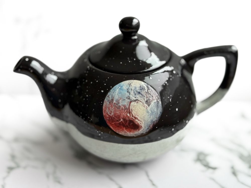 Teapot featuring Pluto surrounded by stars over a landscape.