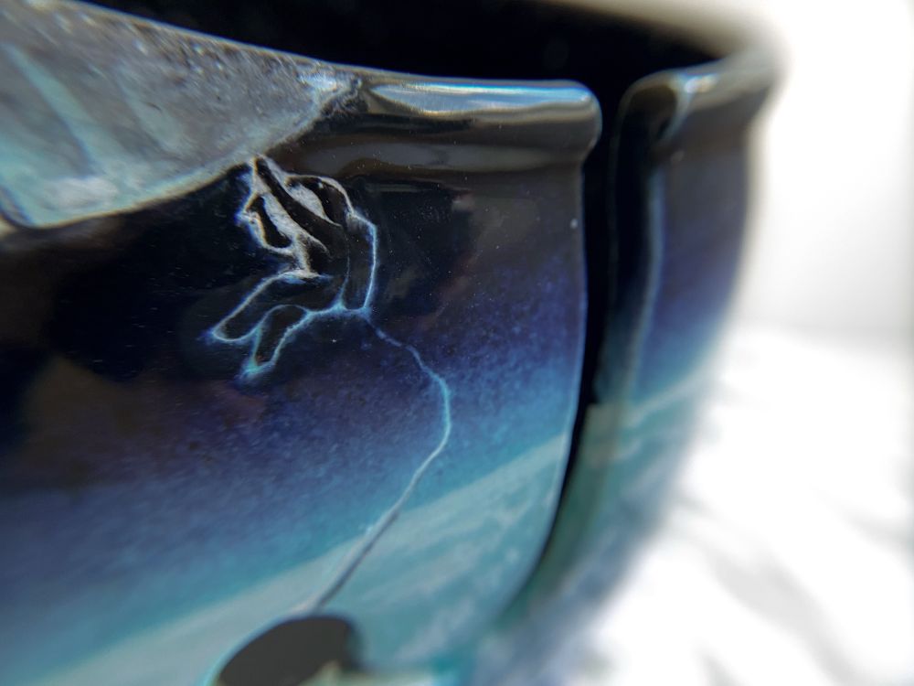 Detail of a yarn bowl showing an astronaut repairing a spacecraft above them and attached to a tether that leads to the yarn feed. 