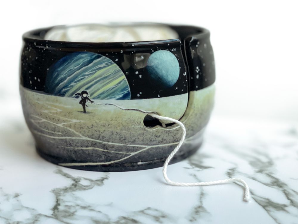 Yarn bowl featuring exoplanets over a barren landscape with an astronaut chasing a tether that leads to the yarn feed.
