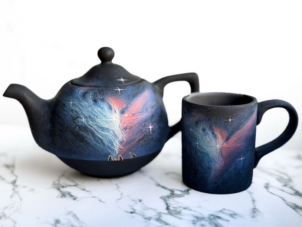 Teapot and mug featuring NGC 2313, teapot has a landscape with a couple people around a campfire and one looking through a telescope 