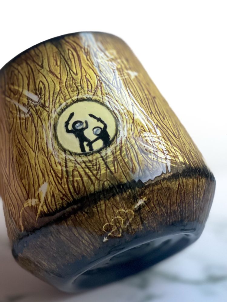 Detail of angled cup: exterior resembles a spacecraft made from wood adorned with space carvings and two hearts with a rocket flying through them at the base. Small round window shows two child astronauts playing with swords inside. 