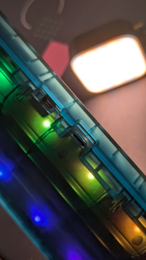 A view from the back of a translucent blue Photon mechanical keyboard. You can see the USB port as well as a switch and the RGB LEDs shining through the case