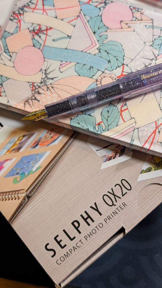 A purple fountain pen sitting on top of a hobonichi weeks journal that is sitting on top of a box. The box is a new Canon Selphy QX20 printer