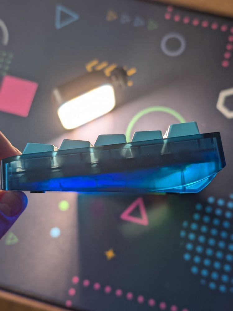 Side profile of a translucent blue Photon mechanical keyboard with a light shining on it to show the translucent nature of the keyboard case