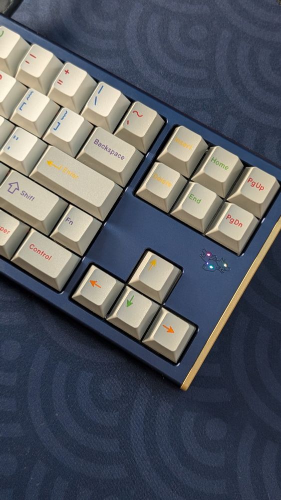 The right side of a navy blue Cerberus keyboard with gold accents and GMK Handarbeige keycaps