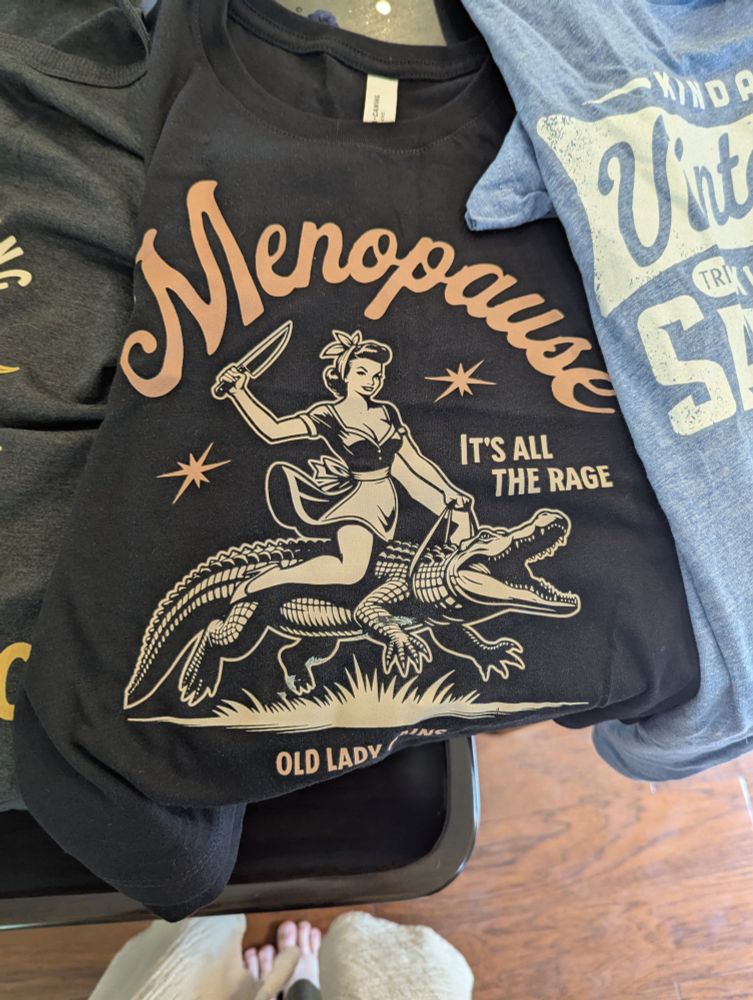 A grey tank with a 50s housewife with a knife riding an alligator reads 