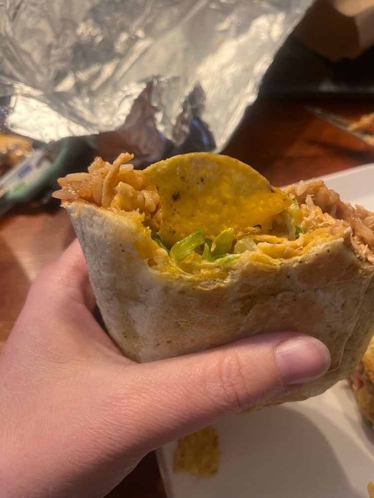 A picture of a hand holding a burrito with a tortilla chip sticking out of it. 