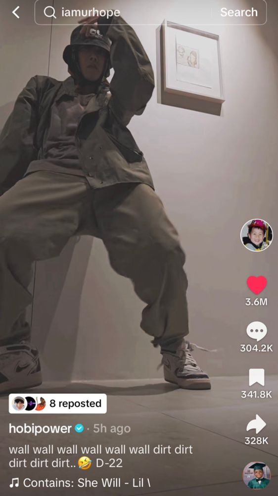 Still frame of J Hope of BTS performing a dance challenge on TikTok, dancing against a wall, and wearing light colored pants, shirt, jacket, high top sneakers, and bucket hat. 