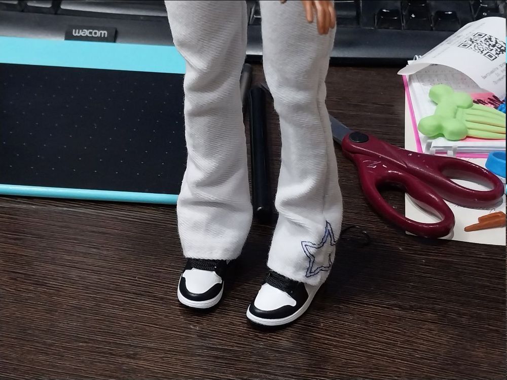 a picture of a fashion doll's legs wearing long white pants widening to the bottom and miniature air jordans (that are too big for her actual small feet)