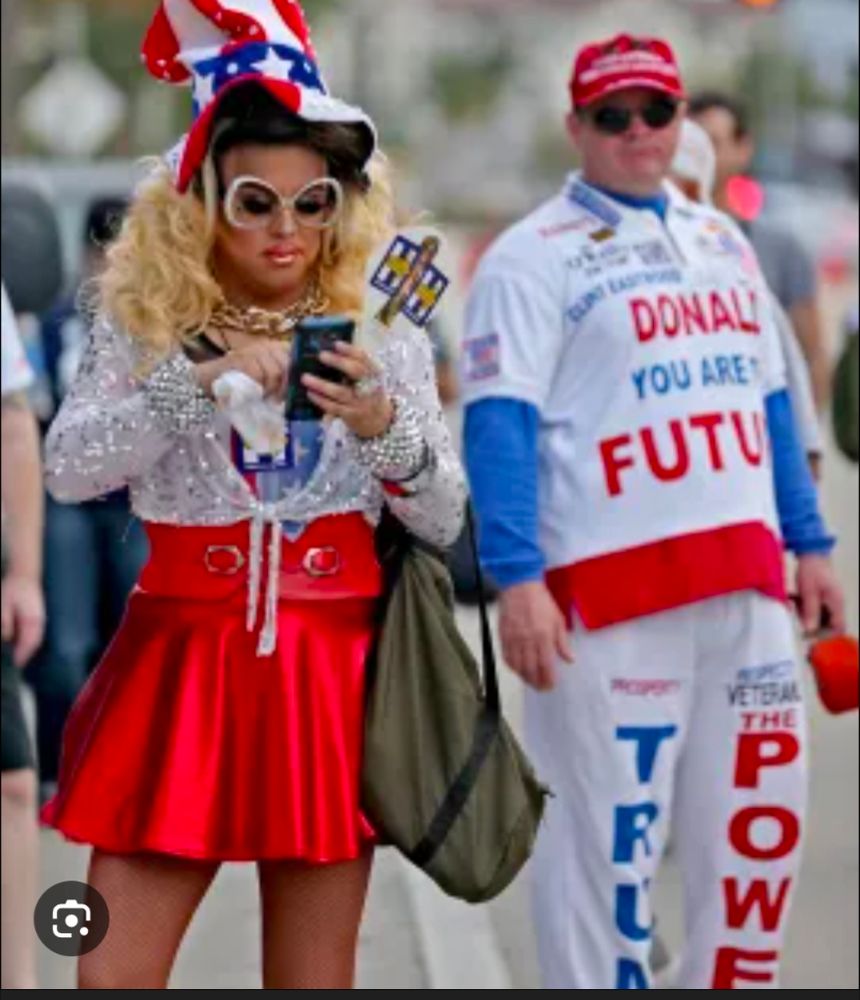 Two felon fans, one in white pajamas, the top a short sleeve white shirt printed with Donald you are the future over a blue long sleeve under shirt. White pants with trump in blue letters down one kg and power in red down the other and a red maga hat. The other dressed in a red silk cheer leaders skirt and top, a white lace long sleeve shrug tied up at midriff, wide fake diamond bracelets, a longish Republican wife blonde wig and a giant red white and blue uncle sam hat with large white rum sunglasses 