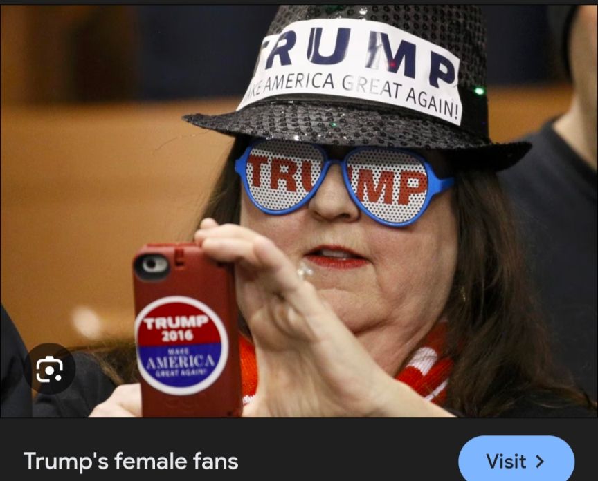 Felon fan with black plastic woven fedora hat with trump maga bumper sticker stuck to the front, wearing glasses that have Tru ump printed over the lenses, holding up a phone with a trump maga 2016 round sticker stuck to the back. Wearing a US flag as a scarf. 