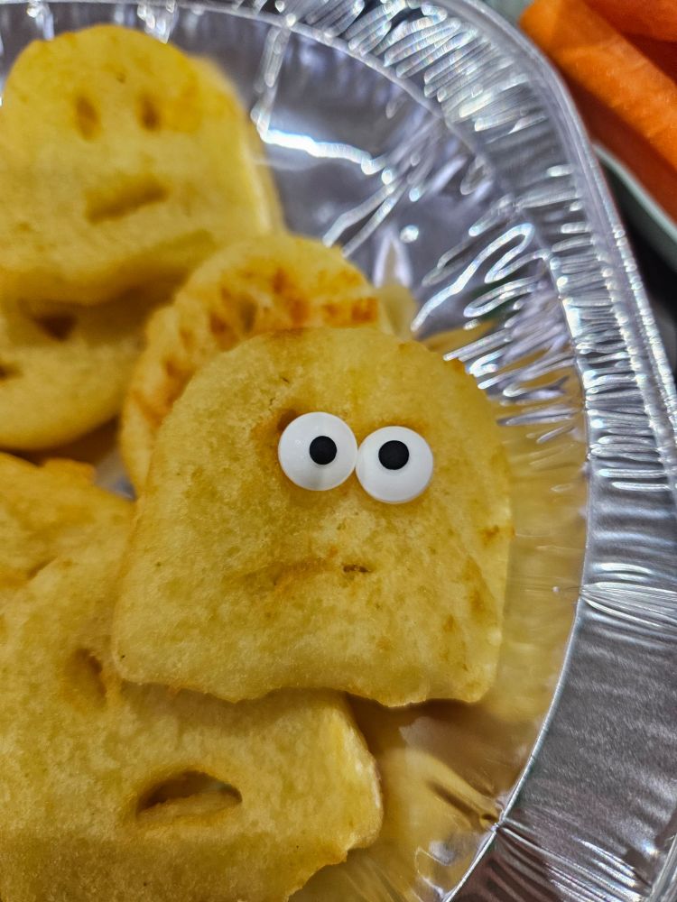 A silver foil plate with some potato ghost smilies. One, the focus of the picture, have sweets for eyes.